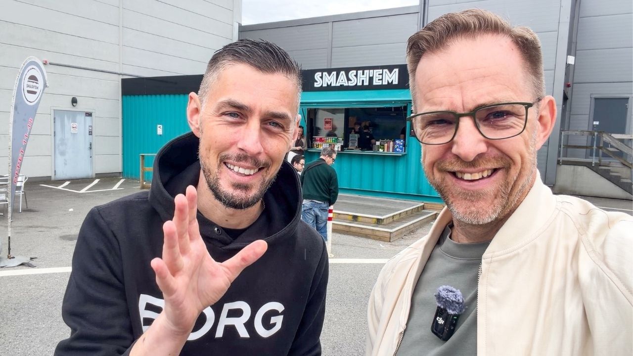Matgeeks två programledare framför Smash'ems turkosa container, med luckan och skylten bakom sig.